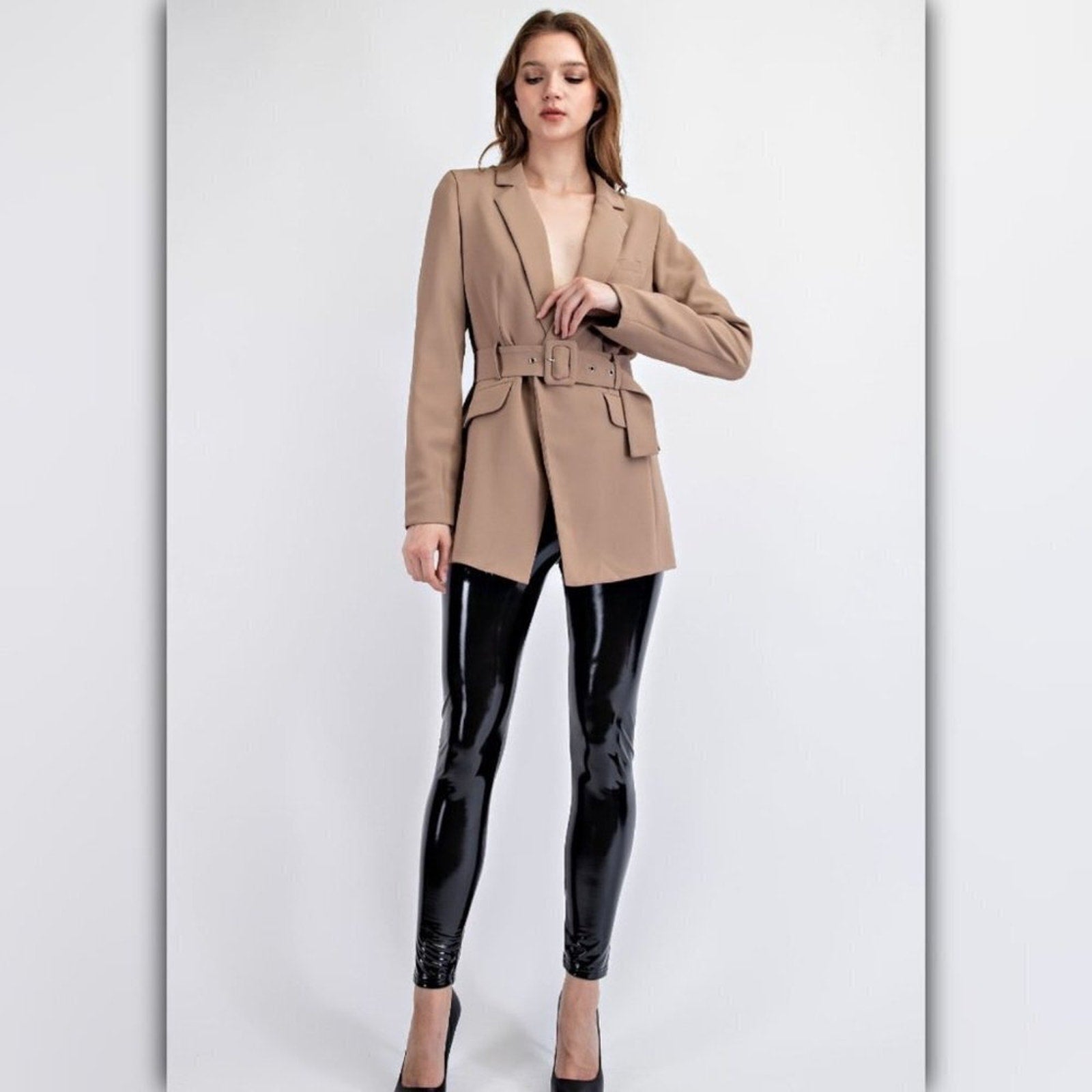 Woman wearing a beige blazer and black vinyl leggings on a white background