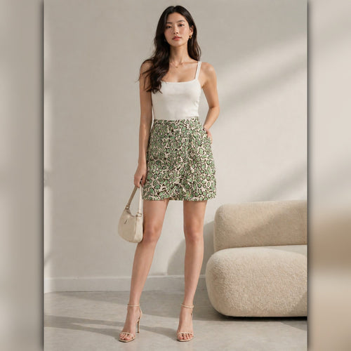 Woman wearing a white top and green floral skirt in a neutral setting