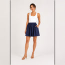 Woman wearing a white tank top and navy blue skirt on a light gray background