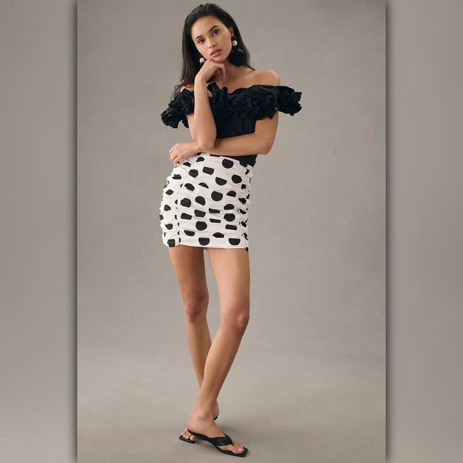Woman wearing a black off-shoulder top and polka dot skirt against a gray background