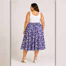 Woman wearing a white tank top and blue floral skirt on a plain background