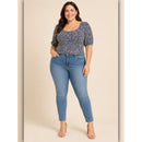 Woman wearing a patterned top and blue jeans on a beige background