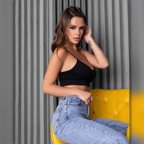 Woman in black top and blue jeans sitting on a yellow chair against a striped wall.
