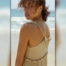 Woman in a beige dress standing on a beach with ocean waves in the background
