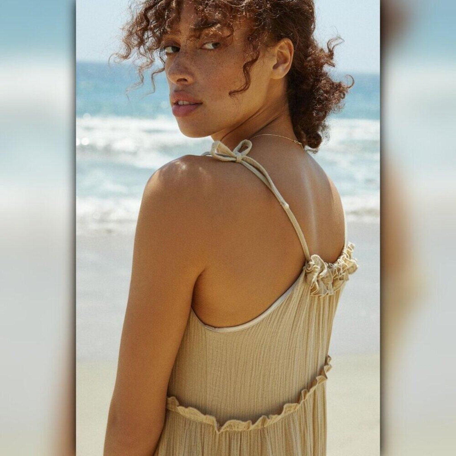 Woman in a beige dress standing on a beach with ocean waves in the background