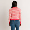 Person wearing a pink and red striped sweater with blue jeans on a plain background