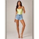 Woman wearing a light green tank top and denim shorts on a plain background