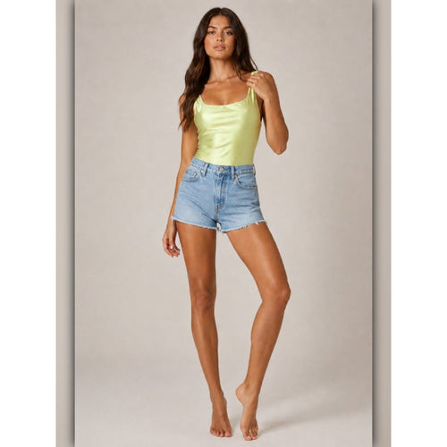 Woman wearing a light green tank top and denim shorts on a plain background