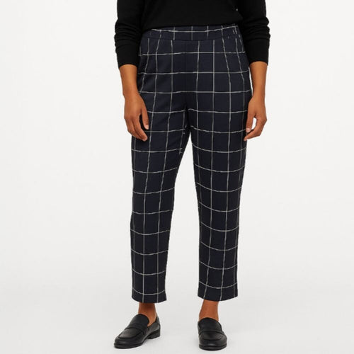 A model wearing navy blue cropped trousers with a white windowpane grid pattern, paired with a black long-sleeve top and black loafers, shown against a plain white studio background.