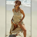 Woman in a beige dress standing on a sandy beach with ocean waves in the background