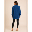 A woman viewed from the back wearing a textured royal blue cable-knit cardigan sweater, black skinny pants, and tan heeled sandals against a solid beige studio background.