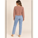 A woman shown from the back wearing a dusty rose cropped long-sleeve knit top and light blue straight-leg jeans, standing against a solid beige studio background.