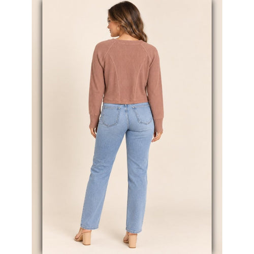 A woman shown from the back wearing a dusty rose cropped long-sleeve knit top and light blue straight-leg jeans, standing against a solid beige studio background.