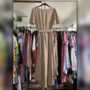 A beige short-sleeve midi dress with a small brown floral print and a matching waist tie, hanging on a black hanger in front of a closet filled with other clothes.