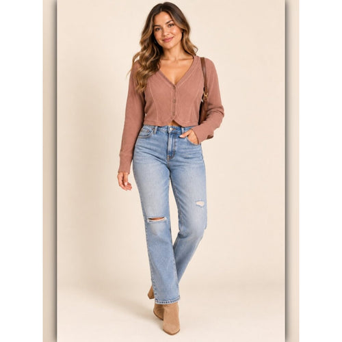 A woman modeling a ribbed knit long-sleeve cardigan in a dusty rose color, paired with light-wash distressed jeans and tan ankle boots, set against a solid beige studio background.