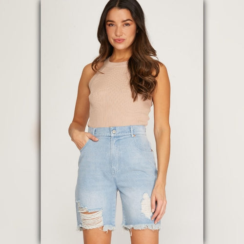 Woman wearing a beige sleeveless top and light blue denim shorts on a plain background