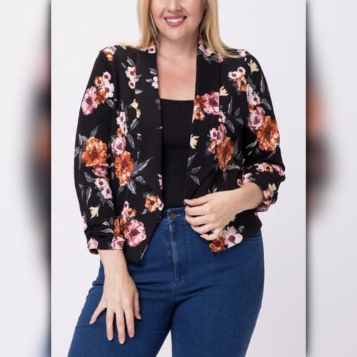 Front close view of plus size model wearing black floral blazer over a black top with blue jeans.