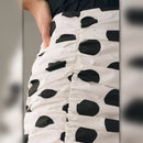 Close-up of a white skirt with black polka dots worn by a person.