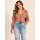 A woman modeling a ribbed knit cropped cardigan in a dusty rose-brown color, paired with light-wash distressed blue jeans, against a solid beige background.