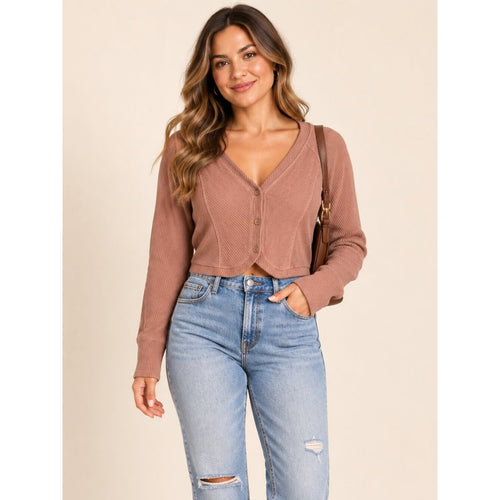 A woman modeling a ribbed knit cropped cardigan in a dusty rose-brown color, paired with light-wash distressed blue jeans, against a solid beige background.