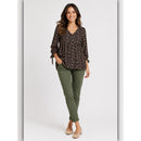Woman wearing a patterned blouse and green pants on a white background