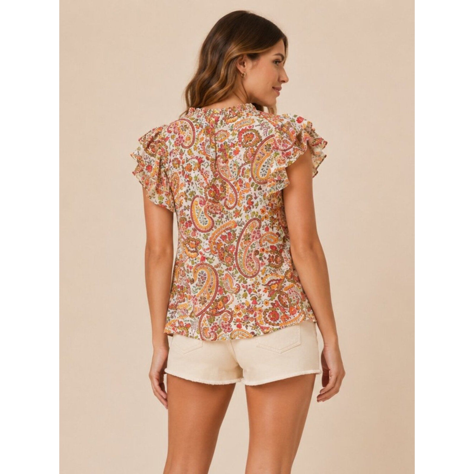 Woman wearing a floral blouse and beige shorts against a beige background