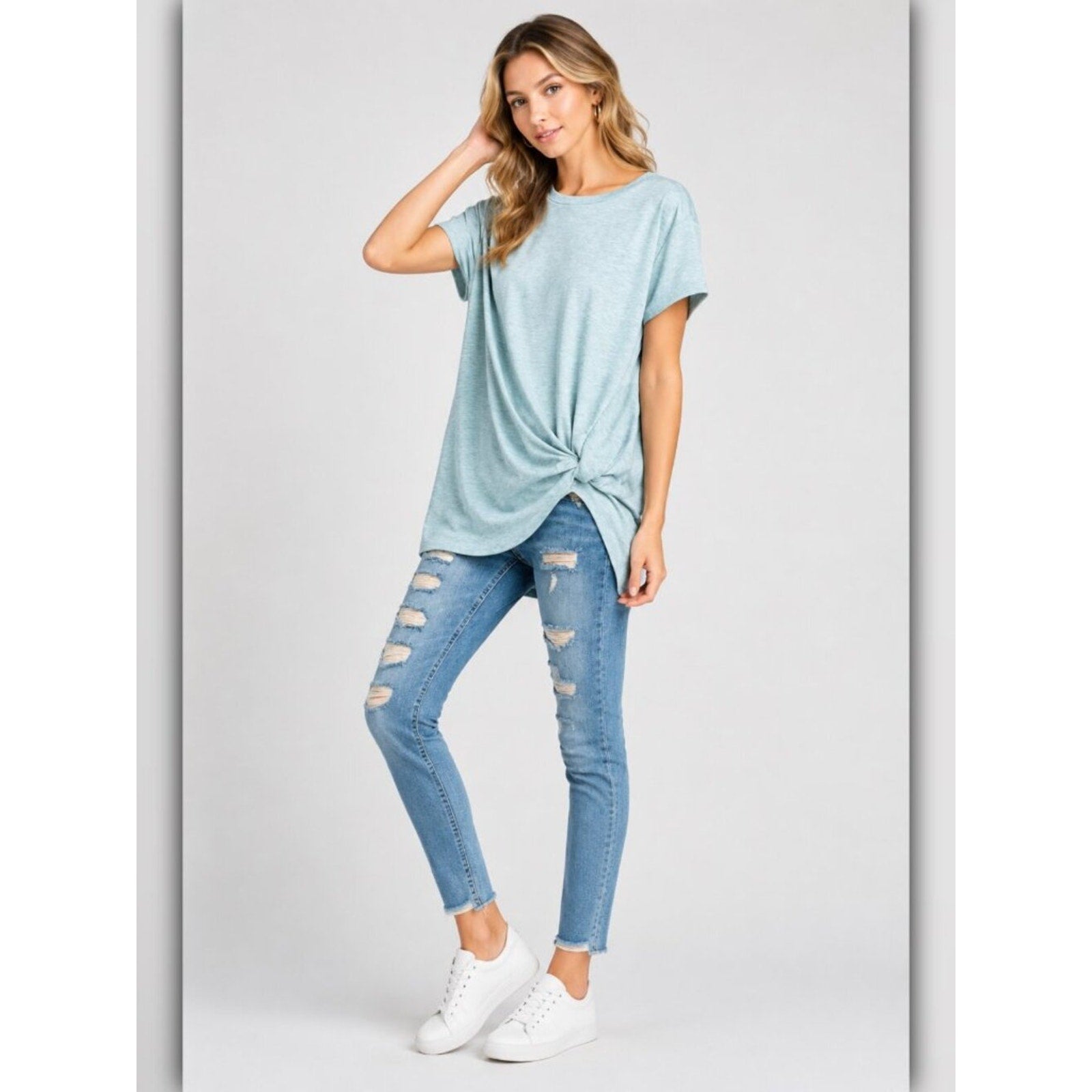 Woman wearing a light blue t-shirt and distressed jeans on a gray background