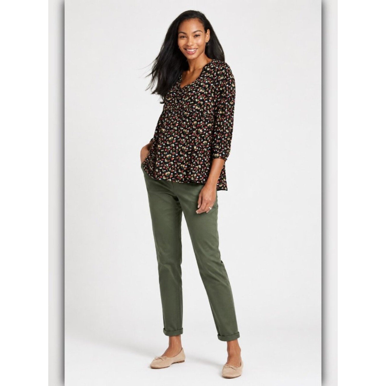 Woman wearing a patterned top and green pants on a white background