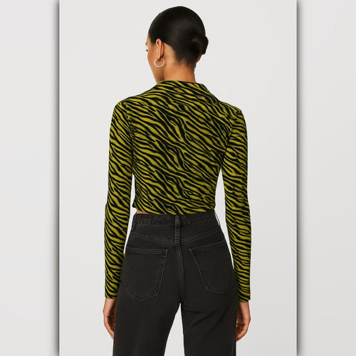 Person wearing a green and black zebra print long-sleeve top with black pants on a light gray background