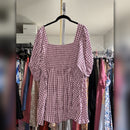 A pink and white gingham puff-sleeve top hanging on a black hanger in a closet with other clothes visible in the background.