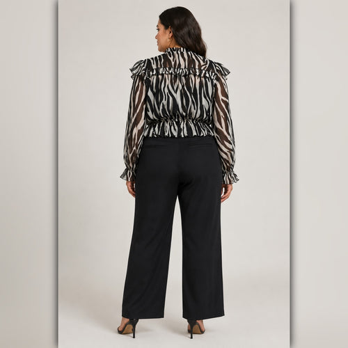 Woman wearing a zebra print blouse and black pants on a plain background