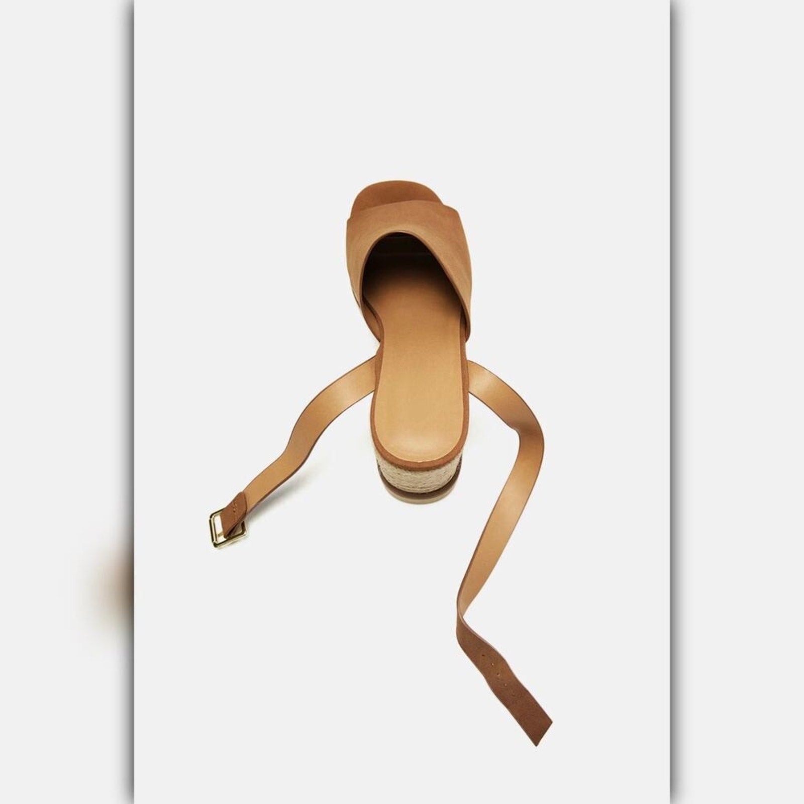 A single tan leather wedge sandal with a long wraparound strap and a small gold buckle, shown from a top-down perspective on a light gray background.