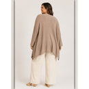 A woman shown from the back wearing a loose, draped taupe knit poncho-style top with wide-leg cream pants and flat sandals, photographed against a plain light studio background.