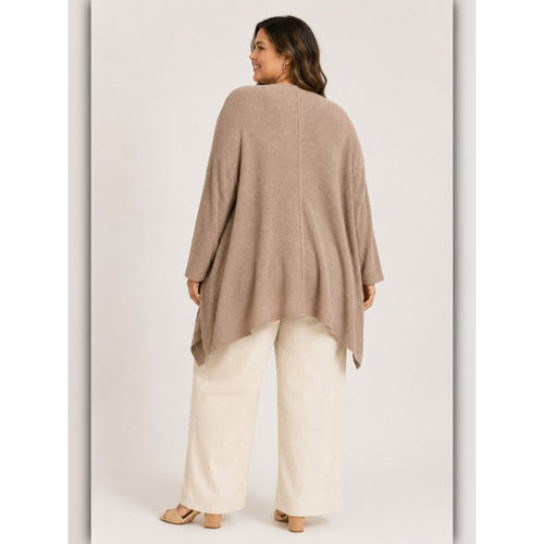 A woman shown from the back wearing a loose, draped taupe knit poncho-style top with wide-leg cream pants and flat sandals, photographed against a plain light studio background.