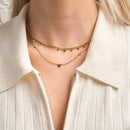 Close-up of a person wearing a gold necklace with a heart pendant on a light-colored shirt.