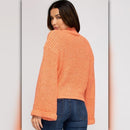 Woman wearing an orange knitted sweater and blue jeans on a plain background