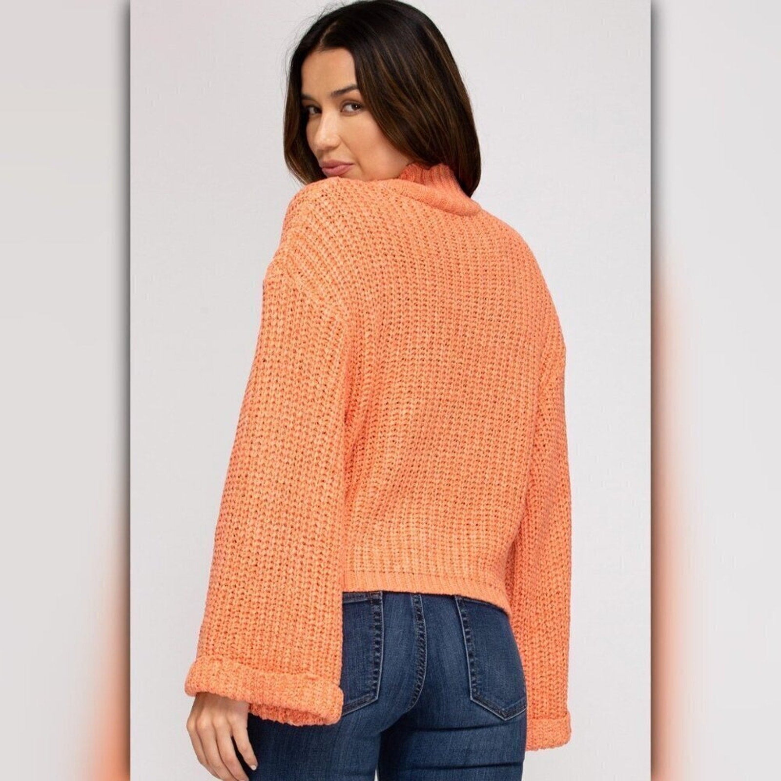 Woman wearing an orange knitted sweater and blue jeans on a plain background