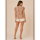 Woman wearing a patterned blouse and white shorts on a beige background