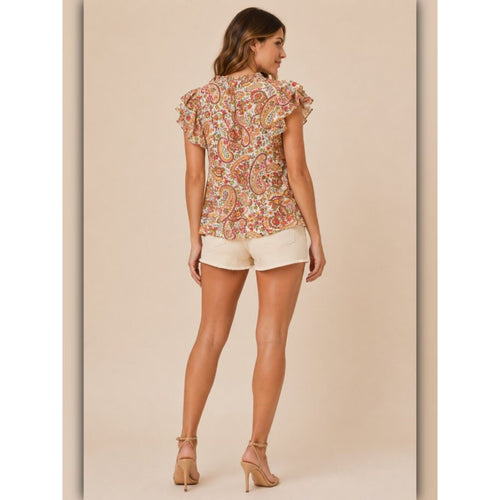 Woman wearing a patterned blouse and white shorts on a beige background