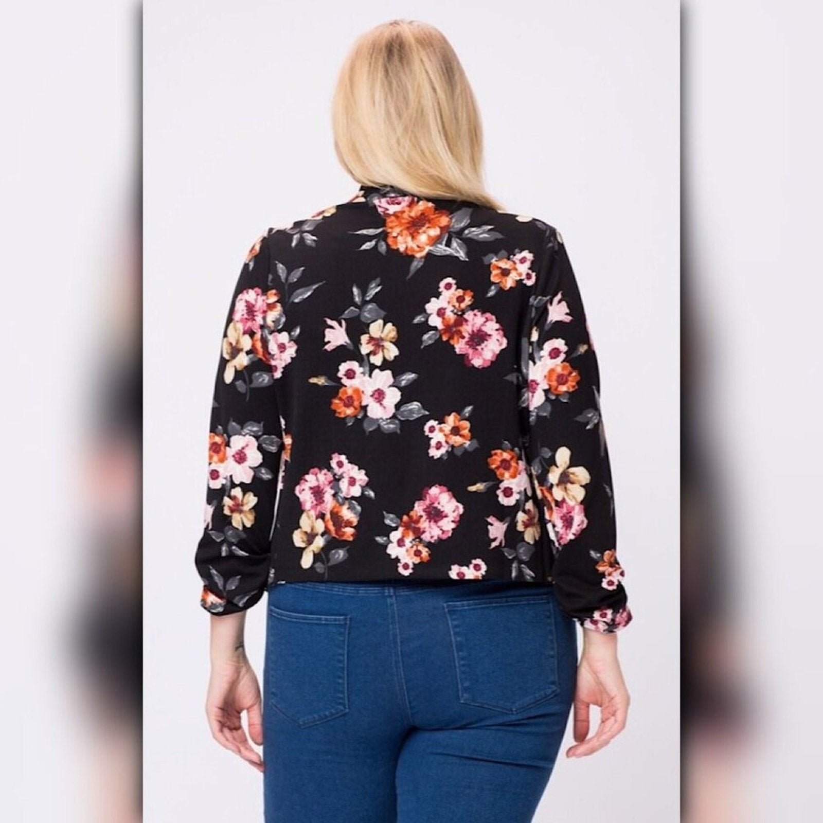 Back view of black floral blazer showing allover pink, orange, cream, and gray floral print on black fabric.