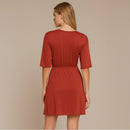 A woman shown from the back wearing a rust-red short-sleeve shift dress with a gathered waist, set against a solid beige studio background.