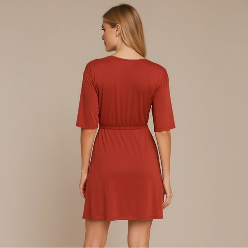 A woman shown from the back wearing a rust-red short-sleeve shift dress with a gathered waist, set against a solid beige studio background.