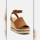 A single women's wedge sandal in tan suede with an ankle strap and gold-tone buckle, featuring a braided jute platform wedge and a light beige sole, shown on a light gray background.