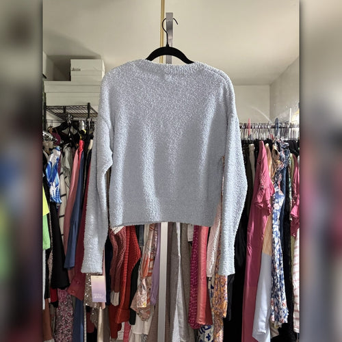 A light gray textured knit long-sleeve crop top hanging on a black hanger in front of a closet rack filled with colorful clothing.