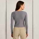 Woman wearing a gray ribbed sweater and beige pants against a plain background
