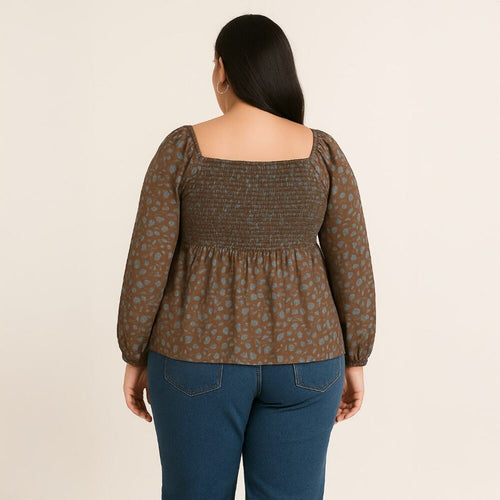 A woman viewed from the back wearing a brown smocked long-sleeve blouse with a muted blue floral pattern and blue jeans, set against a plain off-white background.
