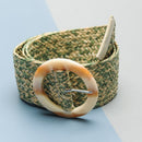 Green woven belt with a large circular buckle on a light blue background