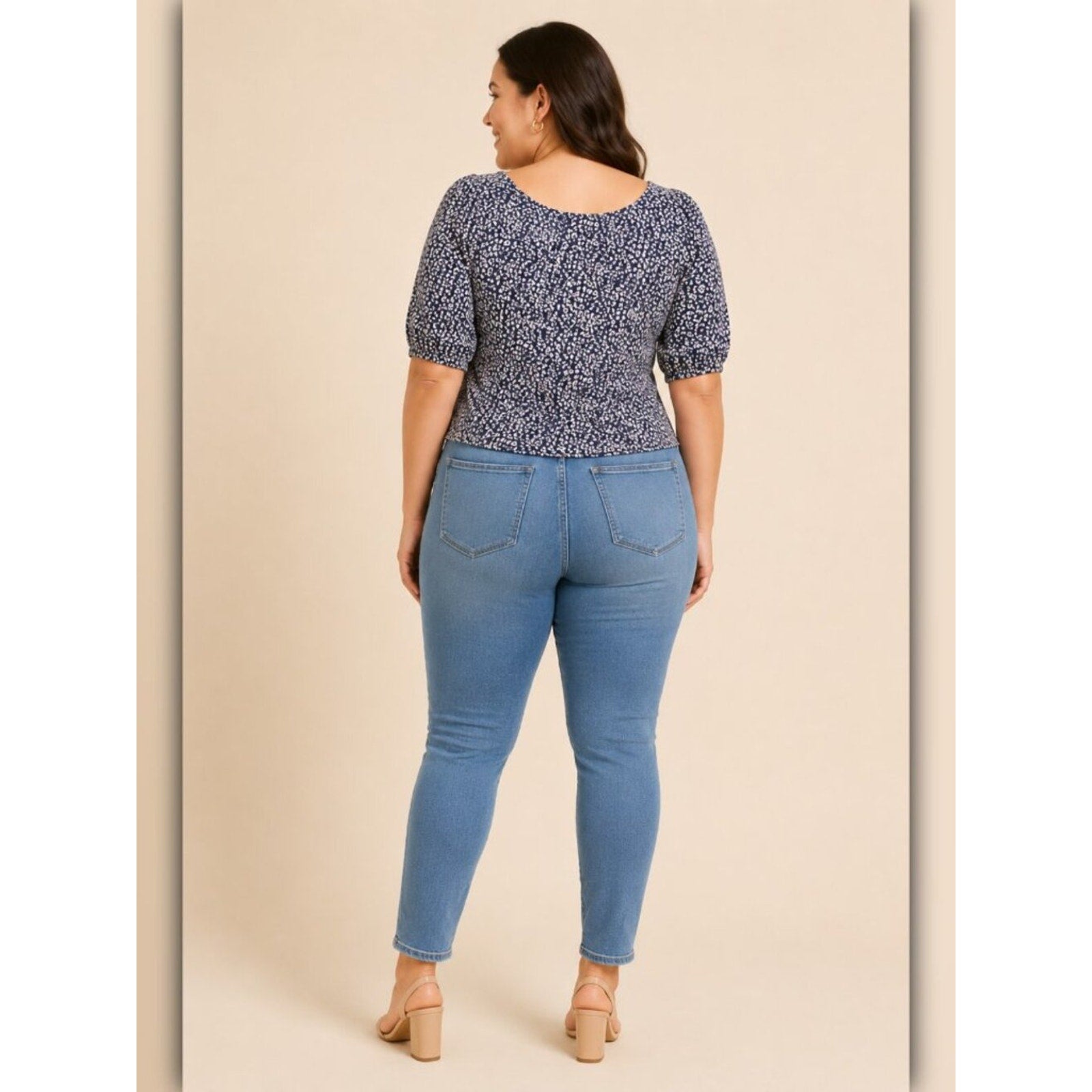 Woman wearing a patterned top and blue jeans on a beige background