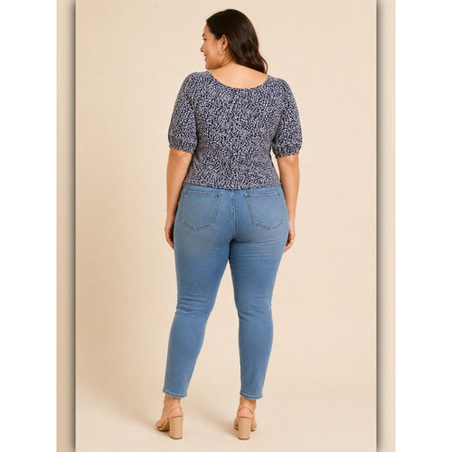 Woman wearing a patterned top and blue jeans on a beige background