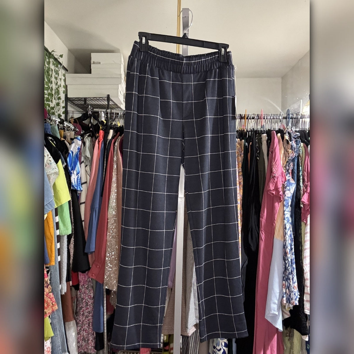 A pair of dark gray wide-leg pants with a white windowpane plaid pattern, hanging on a black hanger in a closet filled with other clothes.